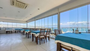 A dining area with tables and chairs, large windows, and a view of the sea. - Dedeoglu Hotel (Fethiye)