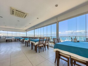 A dining area with tables and chairs, large windows, and a view of the sea. - Dedeoglu Hotel (Fethiye)