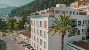A multi-story building with balconies, a palm tree in the foreground, and a street with parked cars. - Dedeoglu Hotel (Fethiye)