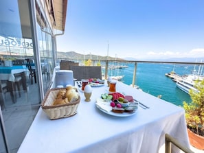 A table with a variety of food items and drinks, overlooking a marina with boats. - Dedeoglu Hotel (Fethiye)