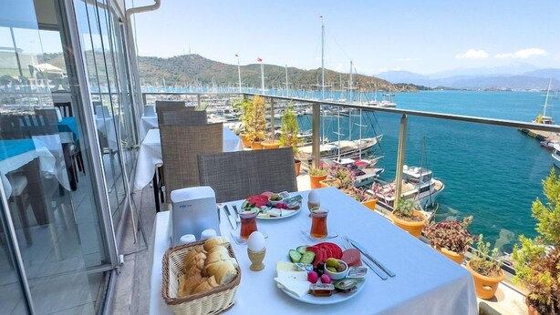 A balcony with a table set for breakfast overlooking a marina with boats and a bridge. - Dedeoglu Hotel (Fethiye)