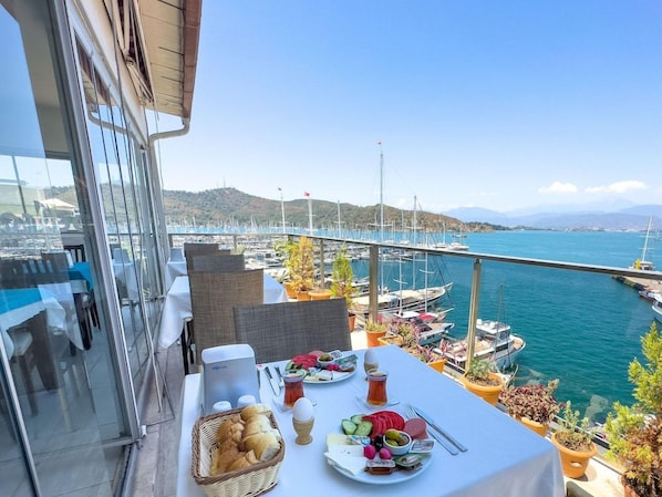 A balcony with a table set for breakfast overlooking a marina with boats and a bridge. - Dedeoglu Hotel (Fethiye)