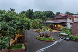 A hotel entrance with a covered walkway, a golf cart, and a landscaped garden with large decorative stones. - Fountain Mahabaleshwar Ihcl Seleqtions (Mahabaleshwar)