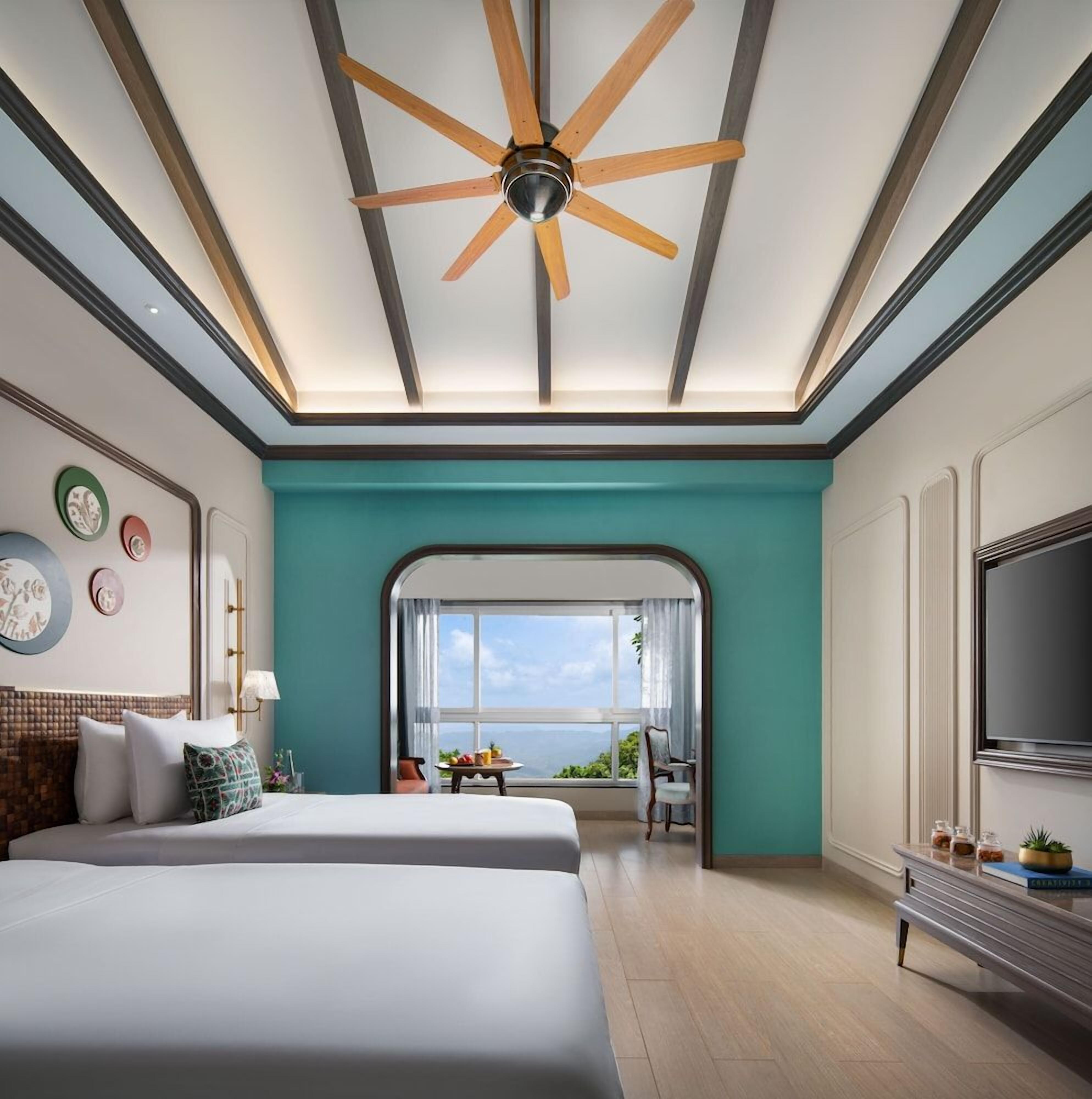 A hotel room with a large bed, a ceiling fan, a TV, and a view of the ocean.