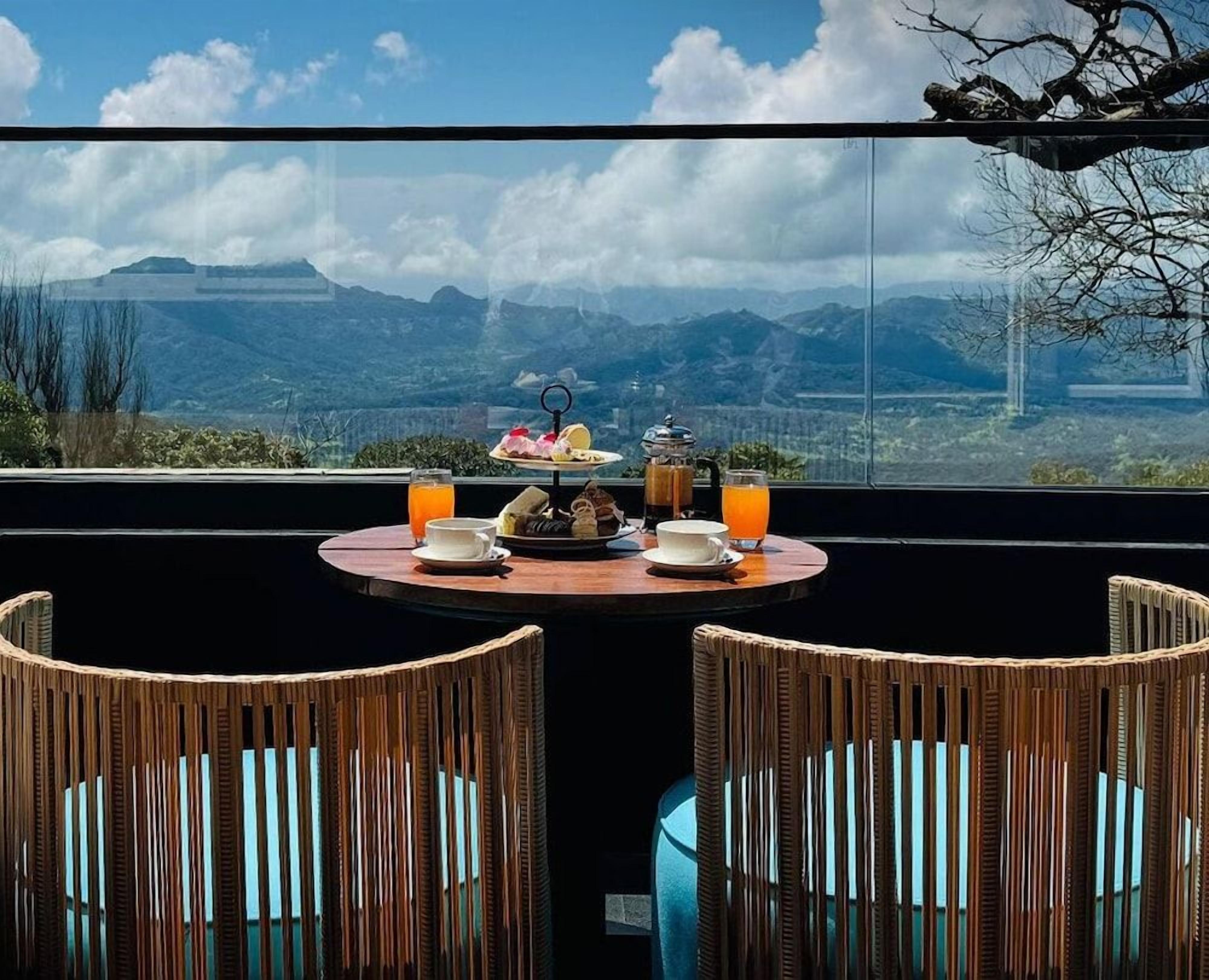 Una mesa con alimentos para el desayuno y un vaso de jugo de naranja, con vistas a un paisaje montañoso.