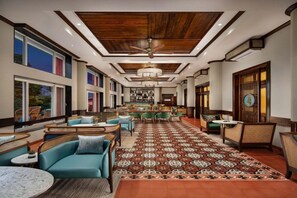 Un vestíbulo de hotel con alfombra estampada, muebles de mimbre y un ventilador de techo.