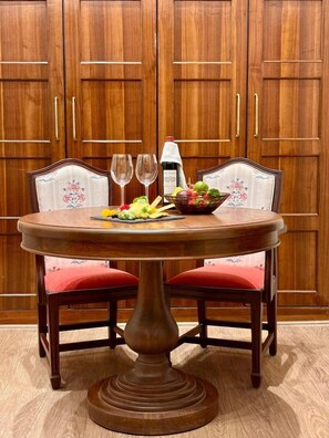 A dining table with a fruit bowl and wine glasses, set against a backdrop of wooden cabinets. - Fountain Mahabaleshwar Ihcl Seleqtions (Mahabaleshwar)