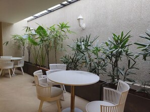 A patio area with round tables and white chairs, surrounded by potted plants and a textured wall. - Olive Hotel Le Opera by Embassy Group (Bengaluru)