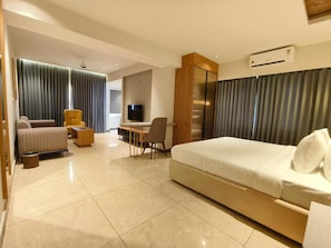 Quarto de hotel moderno com uma cama grande, um sofá, uma escrivaninha e uma televisão.