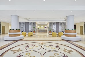 Eine Hotelhalle mit Marmorboden, zwei großen Säulen und einem Empfangstresen im Hintergrund.