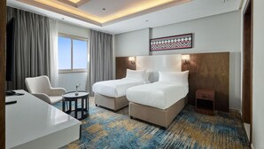 A hotel room with two beds, a desk, a chair, a small table, and a large window. - Nur Al Naseem by Makarem (Makkah)