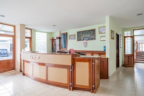 Zona de recepció d'hotel amb un taulell de fusta, una finestra gran i una escala que puja a un altre pis.