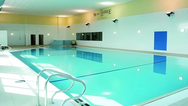 Ein Hallenschwimmbad mit transparenter Decke, einem Schild an der Wand und einer blauen Akzentwand.