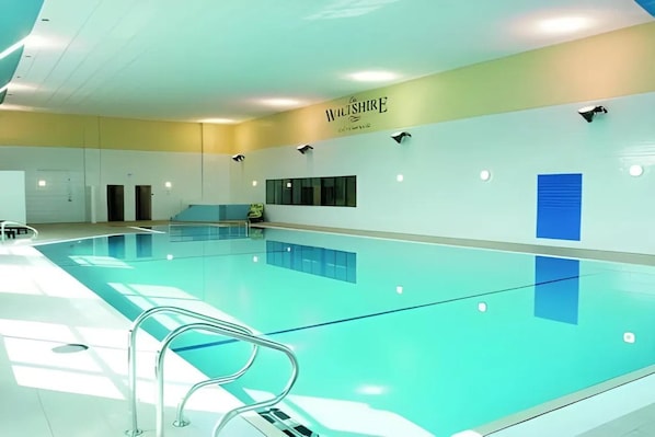An indoor swimming pool with a clear ceiling, a sign on the wall, and a blue accent wall. - The Wiltshire Hotel, Golf & Leisure (Swindon)