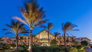 Un hotel a più piani con un cortile centrale, circondato da palme e illuminazione esterna.