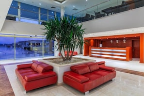 Una hall moderna con una reception, divani rossi e una grande pianta da interno.