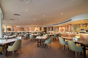 Un'ampia sala da pranzo con diversi tavoli e sedie, un bancone centrale e un moderno design del soffitto.