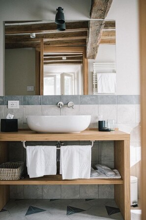 A bathroom with a large white vessel sink, wooden vanity, and a mirror above. - Roncolo 1888 (Quattro Castella)