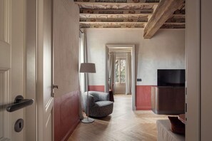 A hallway with a modern chair, a floor lamp, and a television on a cabinet.