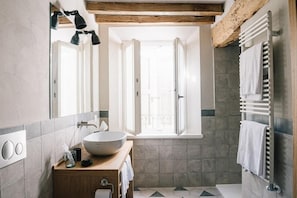 A bathroom with a large mirror, a wooden vanity, a white sink, and a towel rack. - Roncolo 1888 (Quattro Castella)