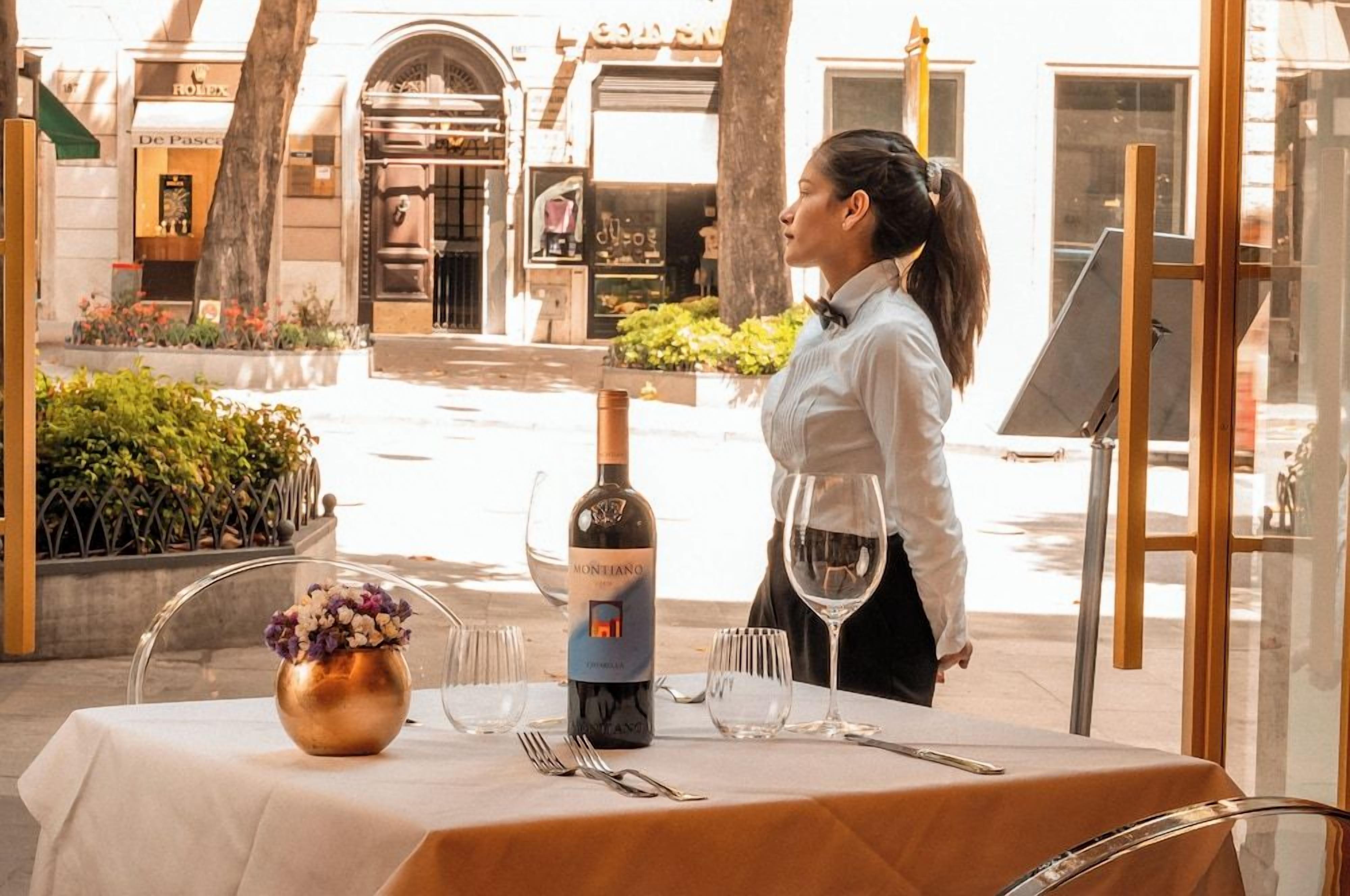 Une table dressée à l’extérieur, avec une bouteille de vin, des verres et des couverts.