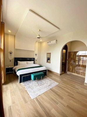 Un dormitorio con cama, mesitas de noche, un banco, un ventilador de techo y un arco de entrada.