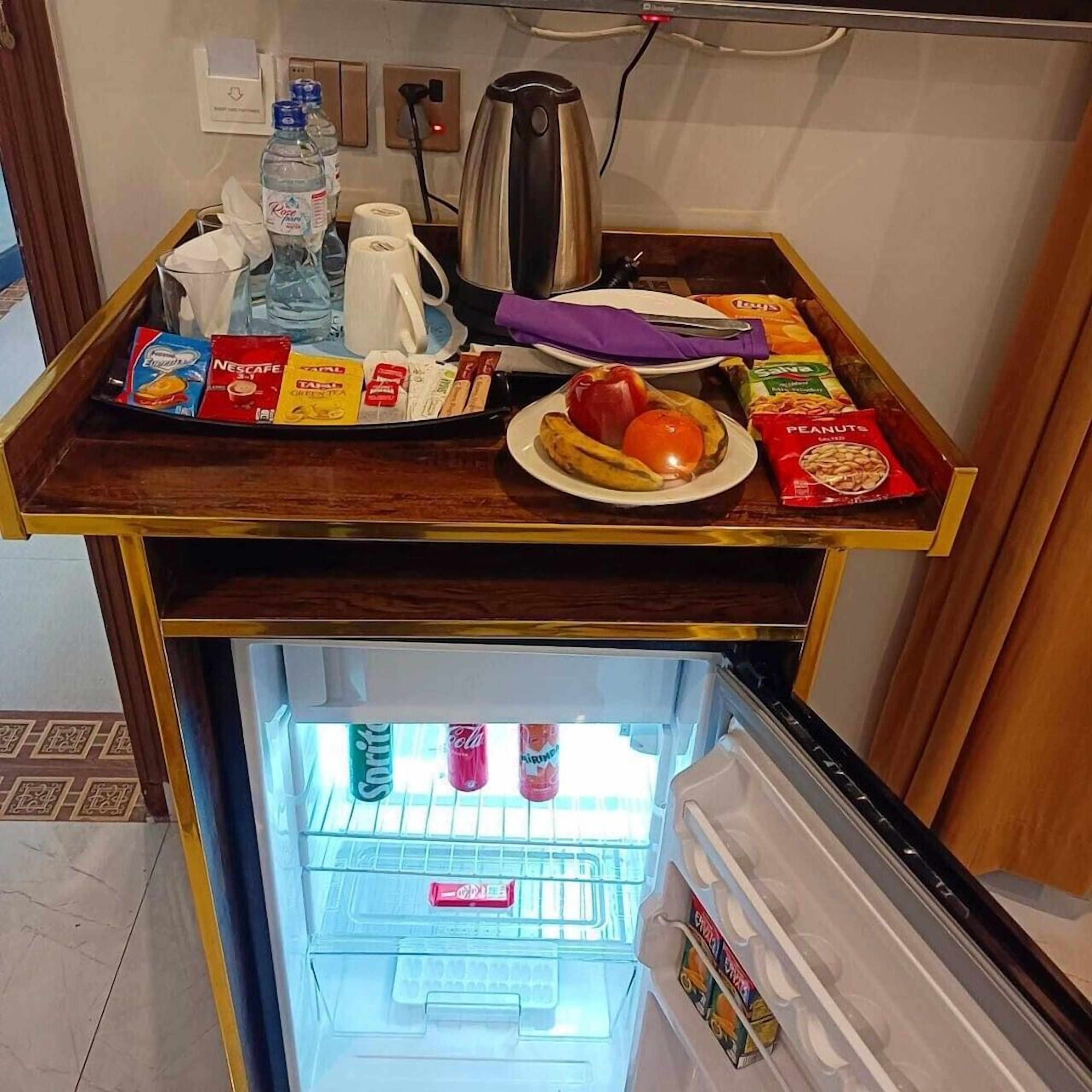 A kitchenette with a coffee maker, kettle, and a tray with food items and beverages.