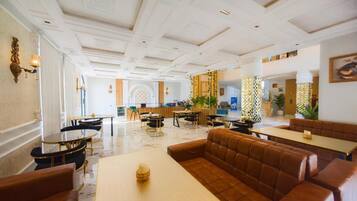 Um saguão de hotel com área de estar central, mesas e uma parede decorativa.