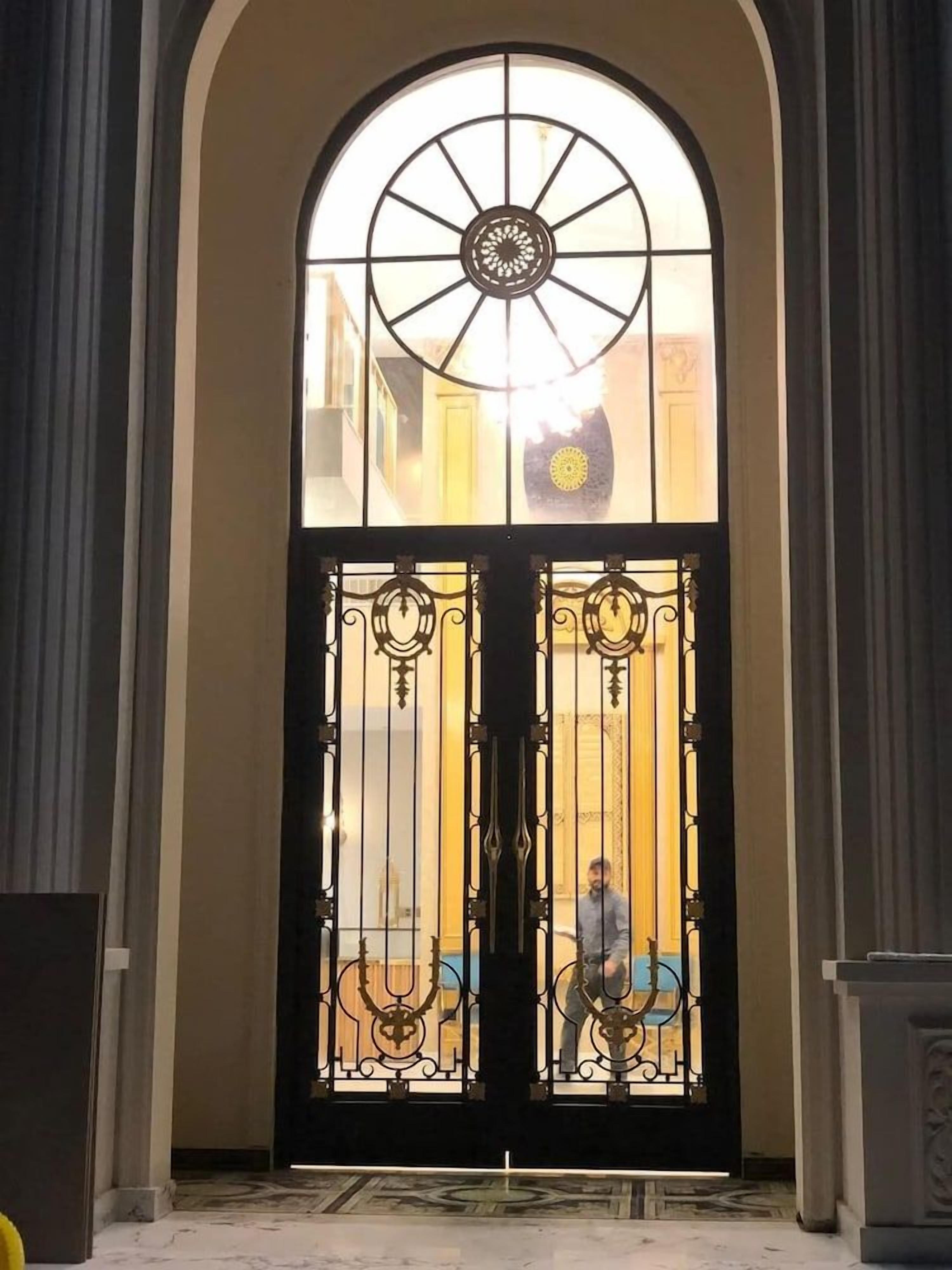Puertas dobles con ornamentación metálica intrincada y un amplio ventanal en arco encima.