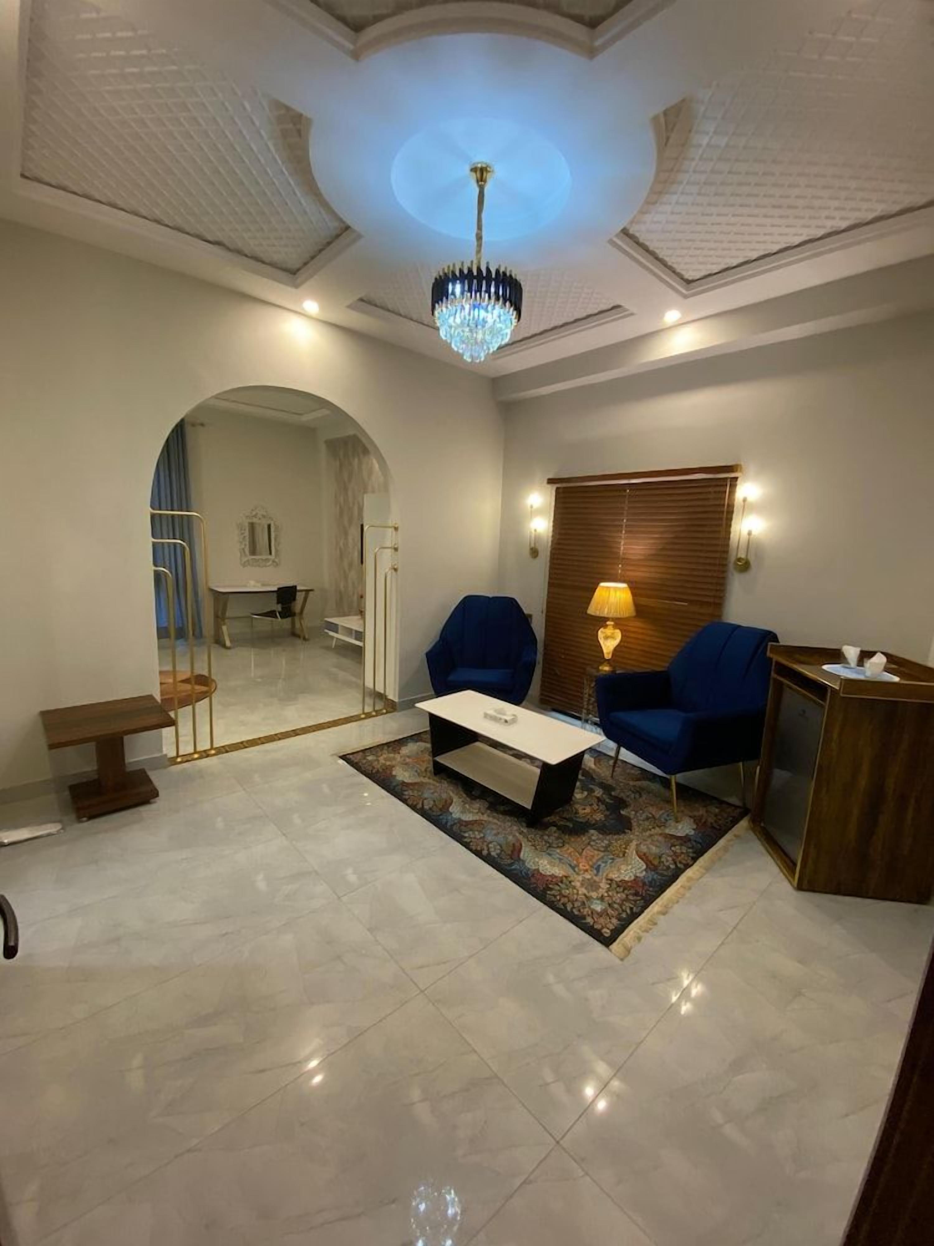 Una sala de estar moderna con una araña, dos sillones azules, una mesa de centro y una mesita de noche de madera.