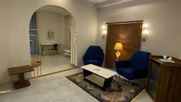 Una sala de estar moderna con una araña, dos sillones azules, una mesa de centro y una mesita de noche de madera.