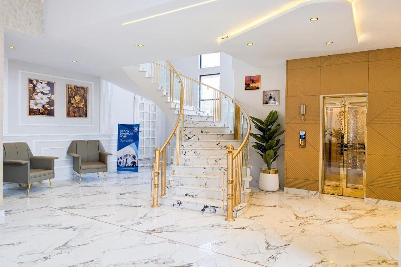 Un vestíbulo de hotel con una escalinata de mármol, zona de estar y mostrador de recepción.