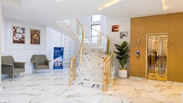 Un vestíbulo de hotel con una escalinata de mármol, zona de estar y mostrador de recepción.