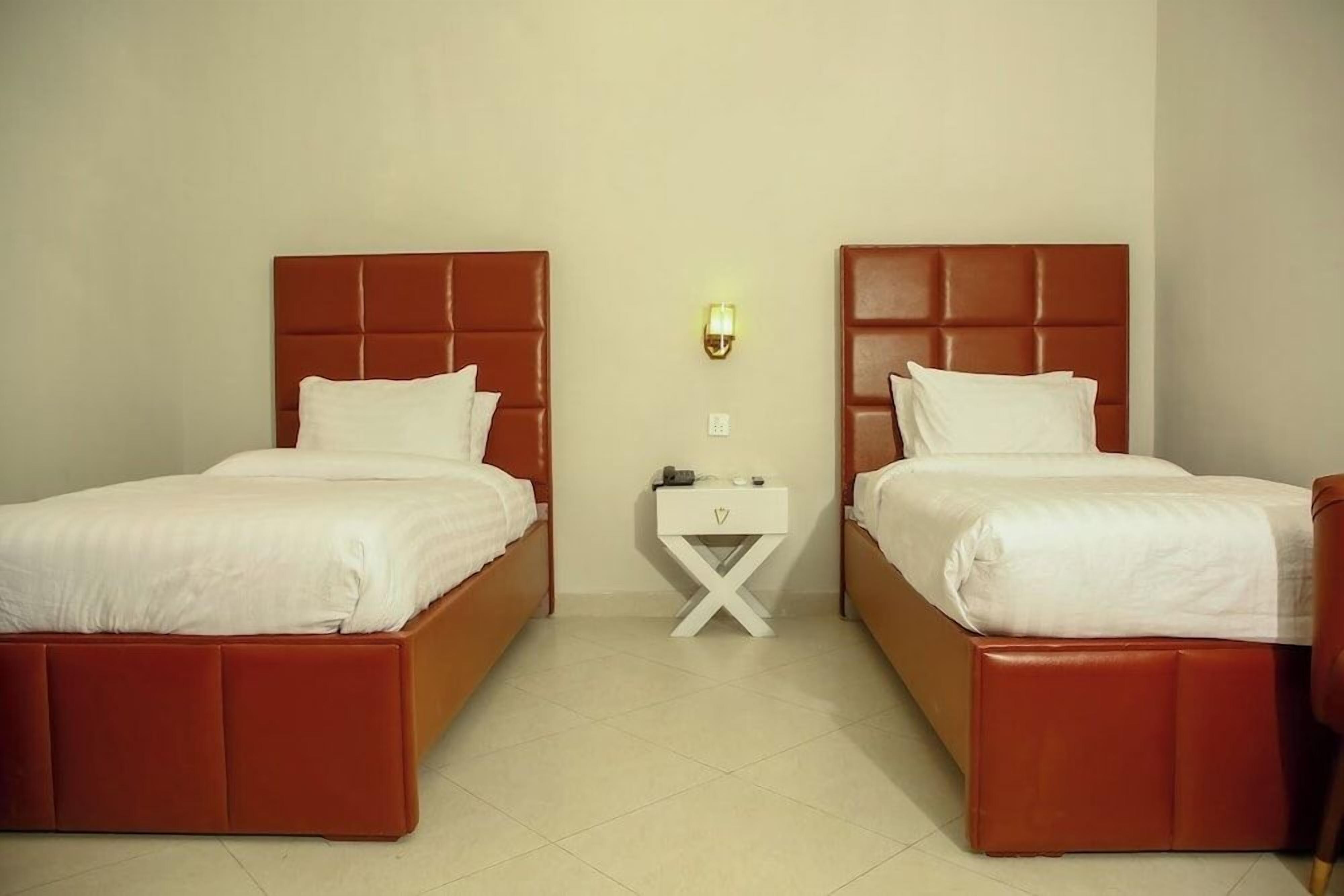 Habitación de hotel con dos camas, una mesita de noche y un aplique de pared.