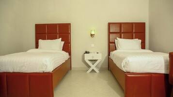 Habitación de hotel con dos camas, una mesita de noche y un aplique de pared.