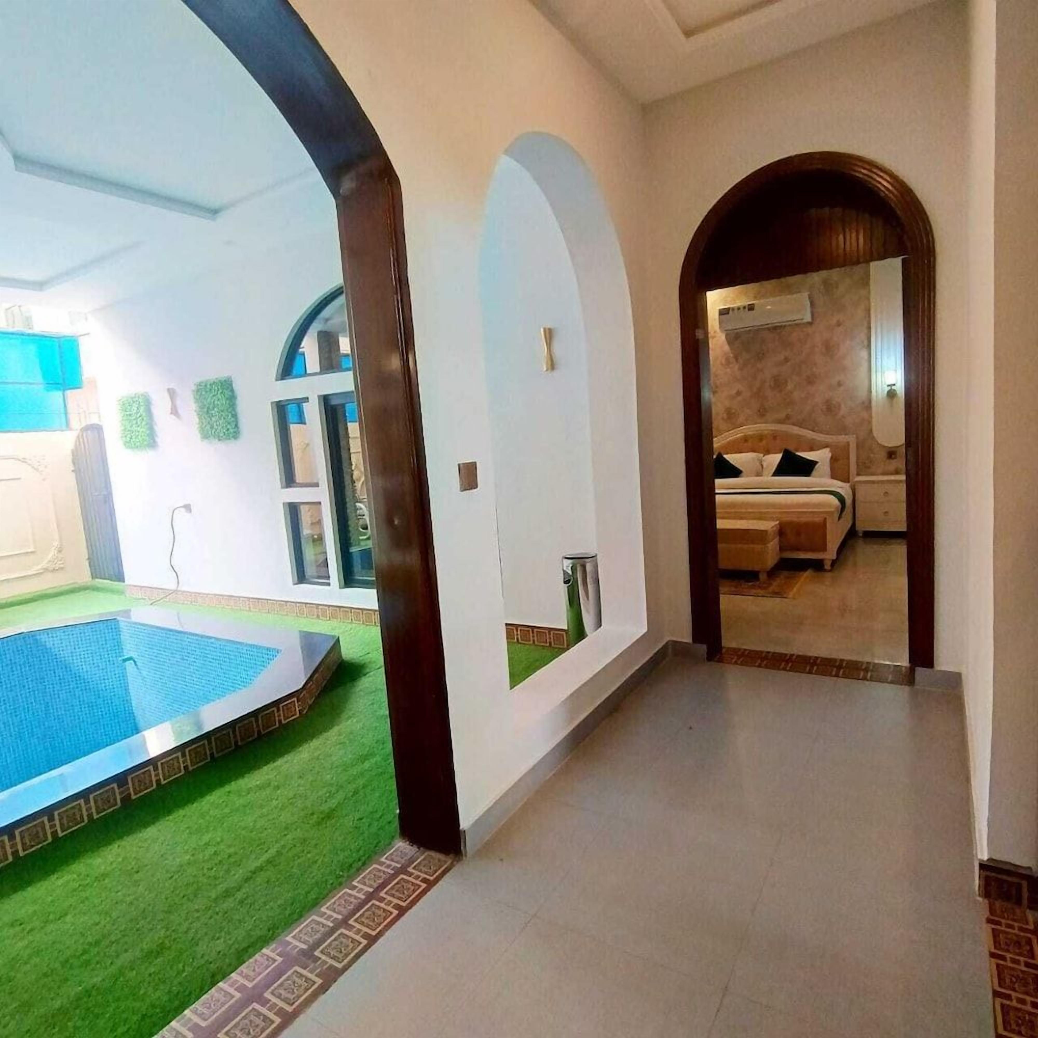 Un pasillo de hotel con zona de piscina, un dormitorio con cama y mesita de noche, y un baño con inodoro y lavabo.