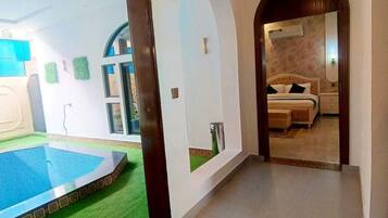 Un pasillo de hotel con zona de piscina, un dormitorio con cama y mesita de noche, y un baño con inodoro y lavabo.