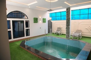 A swimming pool with a tiled edge, surrounded by artificial grass, and two lounge chairs. - Grand Shalimar Hotel (Multan)