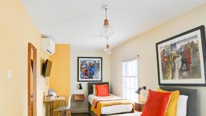 Quarto de hotel com duas camas, uma escrivaninha, uma cadeira e uma janela grande.