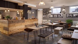 Um interior moderno com área de bar em madeira, diversas mesas e luminárias pendentes.