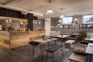 Un interno moderno con una zona bar in legno, diversi tavoli e lampade a sospensione.