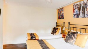 Quarto de hotel com cama, mesa de cabeceira, abajur e parede com pôster.