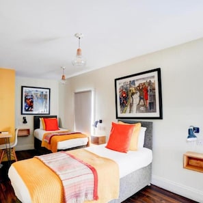 Camera d'albergo con due letti, una scrivania, una sedia, un armadio e opere d'arte alle pareti.