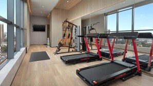 Ein modernes Fitnessstudio mit Laufbändern, Kraftgeräten und einem großen Fenster mit Blick auf die Stadt.