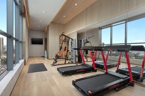 Un gimnasio moderno con cintas de correr, máquinas de pesas y un amplio ventanal con vista a la ciudad.