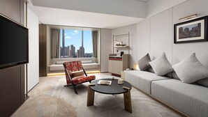 Ein modernes Hotelzimmer mit Sofa, Sessel, Couchtisch, Flachbildfernseher und Blick auf die Stadt.