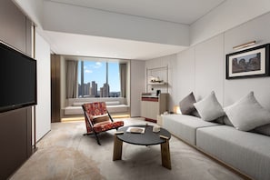 Habitación de hotel moderna con sofá, sillón, mesa de centro, televisión de pantalla plana y vistas a la ciudad.