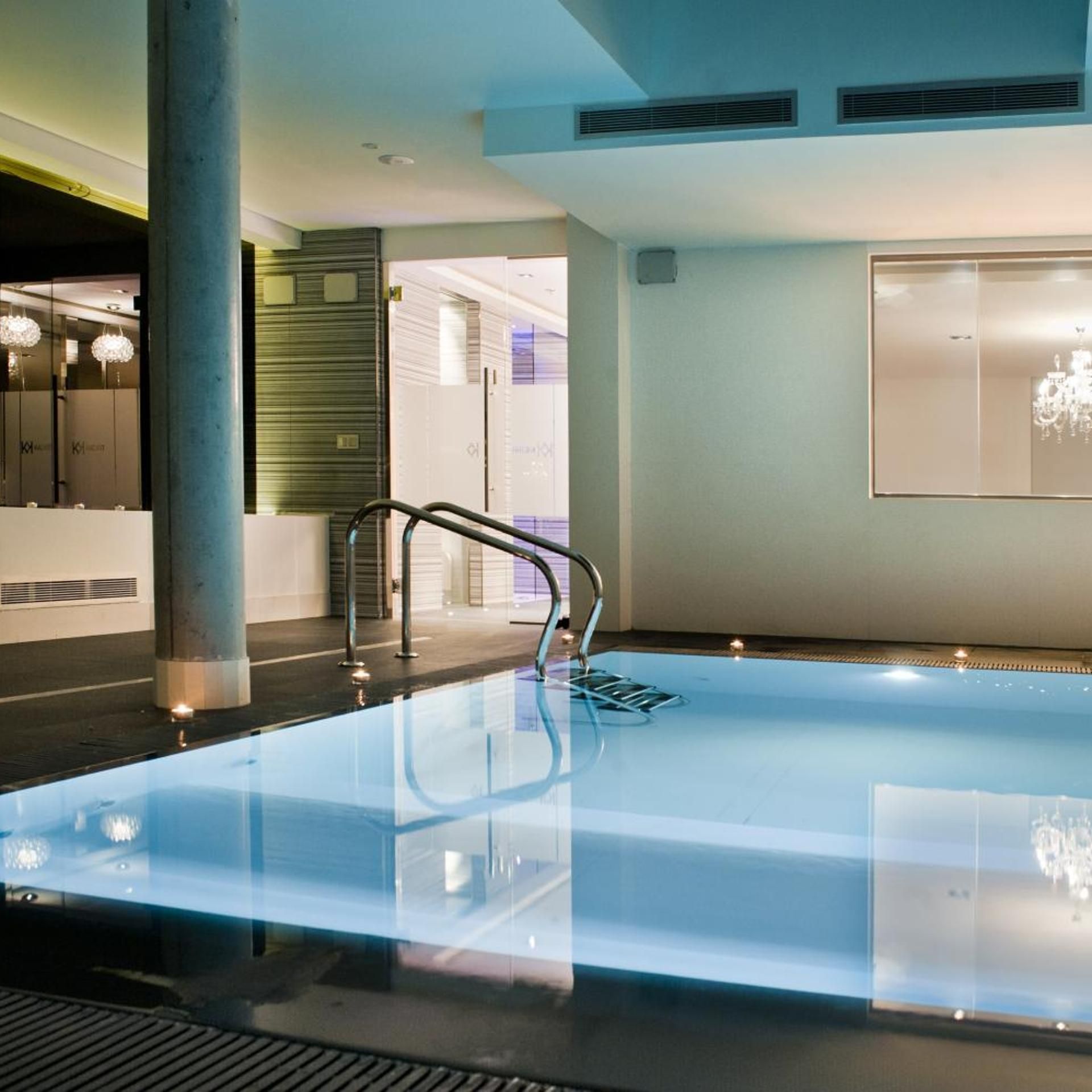 Una piscina interior moderna con fondo de vidrio transparente, barandilla metálica y diseño minimalista.