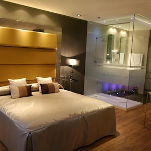 A modern hotel room with a large bed, a glass-enclosed bathroom, and a bedside lamp. - Carretera Valencia km. 13,2 (Cadrete)