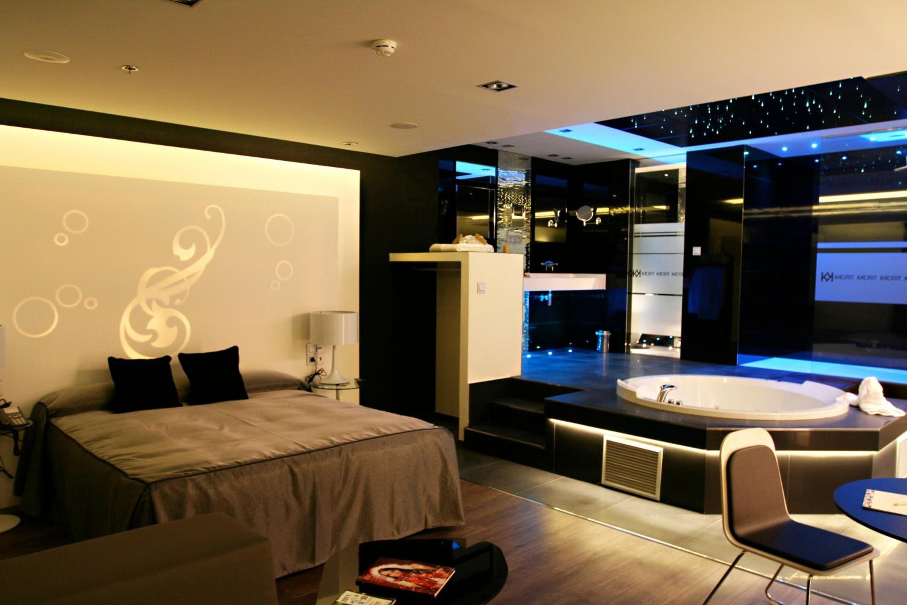 Habitación de hotel moderna con cama, escritorio, silla, espejo grande y baño con bañera.